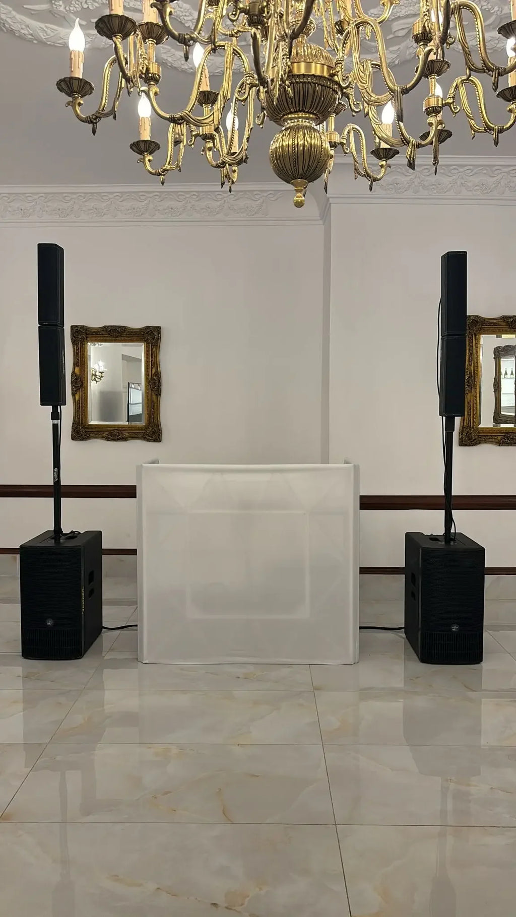 Elegant event setup with black speakers, white DJ booth, and golden chandelier for weddings in Malta.